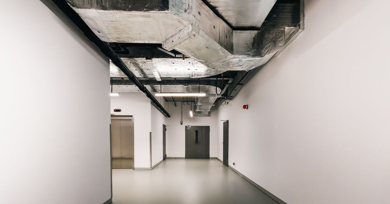 The interior of a commercial building showing exposed ductwork above a corridor